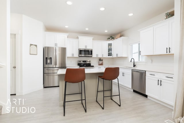 kitchen featuring a kitchen breakfast bar, light wood-type flooring, stainless steel appliances, white cabinets, and a kitchen island