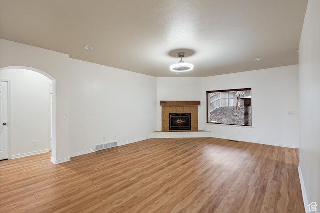 9226 N Mount Airey Dr W, Eagle Mountain, UT 84005 - unfurnished living room featuring light wood-style flooring, arched walkways, baseboards, and a tile fireplace