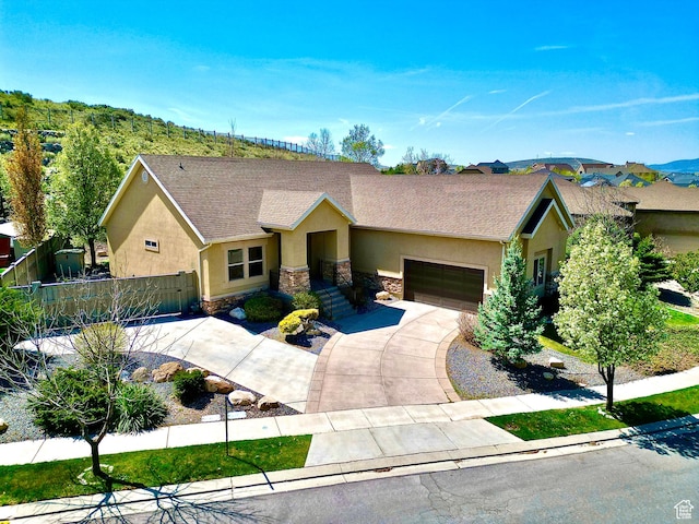 ranch-style house featuring driveway, stone siding, an attached garage, fence, and stucco siding