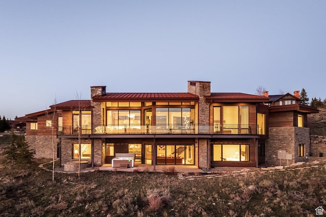 rear view of house with stone siding, a standing seam roof, a chimney, and a balcony