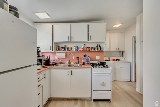 kitchen with light wood finished floors, washer and clothes dryer, a sink, white appliances, and open shelves