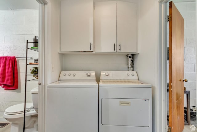 washroom with washing machine and dryer, cabinet space, and concrete block wall