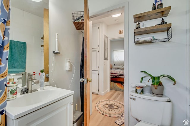 ensuite bathroom with connected bathroom, toilet, vanity, and wood finished floors