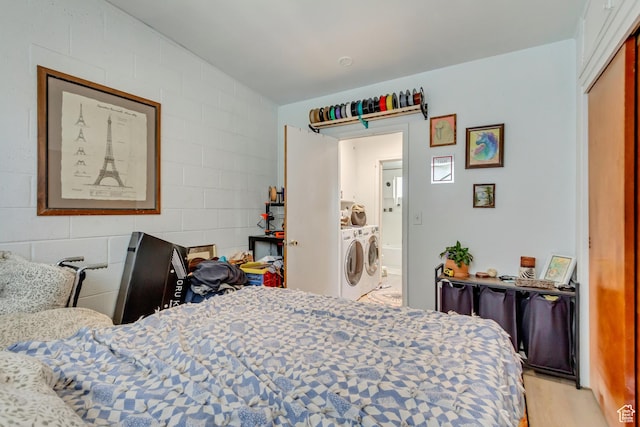 bedroom with light wood-type flooring, concrete block wall, and washer and dryer