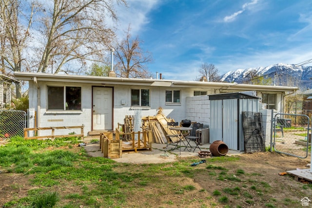 rear view of house with fence, an outdoor structure, concrete block siding, a storage unit, and a mountain view