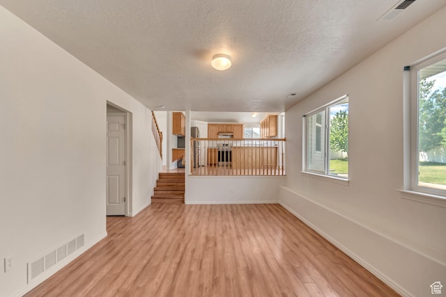 6706 S Adventure Way, West Jordan, UT 84084 - unfurnished living room with light wood finished floors, a textured ceiling, a wealth of natural light, and visible vents