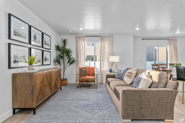 living area with light wood-style flooring, baseboards, a wealth of natural light, and a textured ceiling