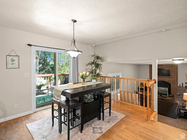 dining room with a brick fireplace, a textured ceiling, light wood finished floors, and baseboards