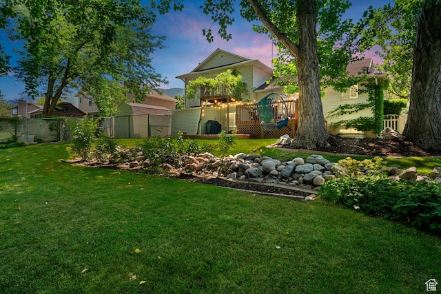 yard at dusk featuring a wooden deck and fence