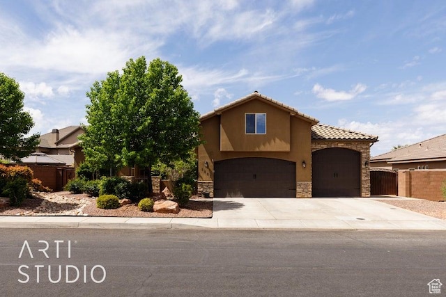mediterranean / spanish home featuring fence, stucco siding, driveway, stone siding, and a garage