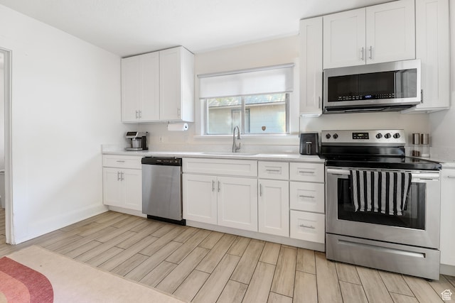 kitchen with white cabinets, stainless steel appliances, a sink, light countertops, and wood tiled floor