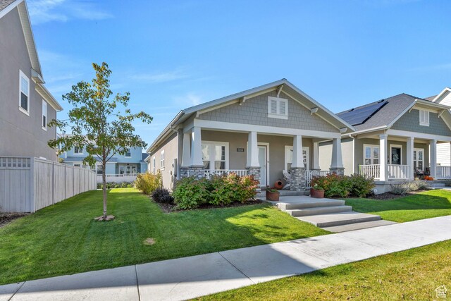 view of front of home with a porch, a front lawn, fence, and solar panels