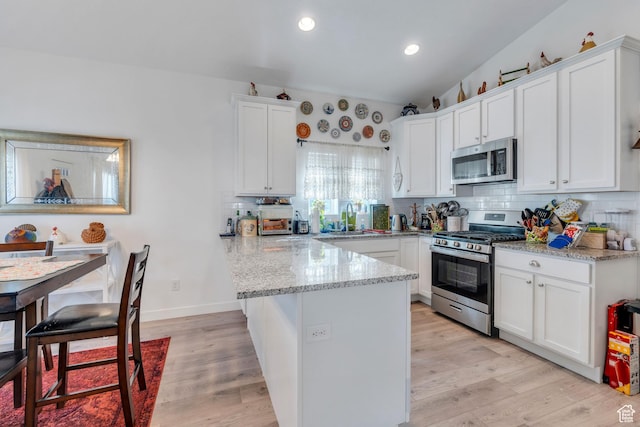 kitchen with light wood finished floors, a peninsula, backsplash, white cabinetry, and appliances with stainless steel finishes