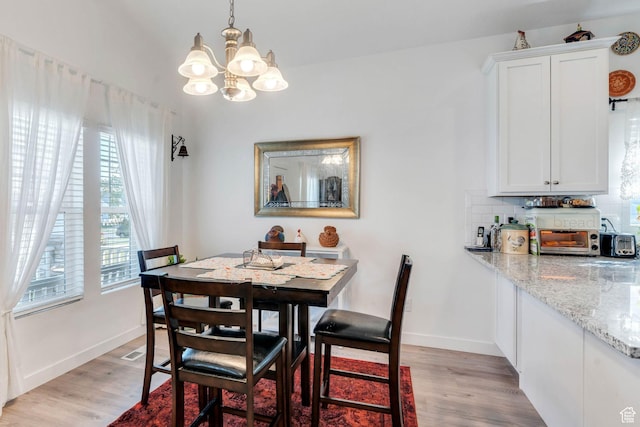 dining room with light wood-style flooring, baseboards, and a notable chandelier