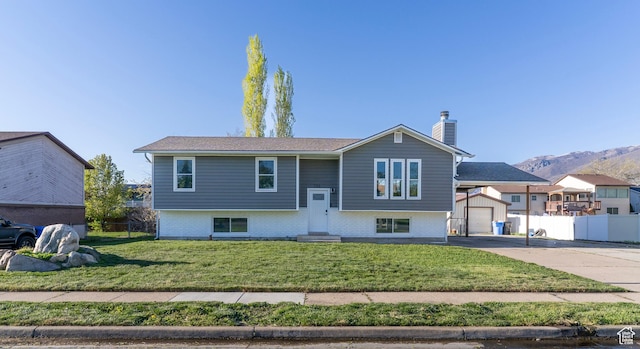 split foyer home with fence, a chimney, concrete driveway, and a front lawn