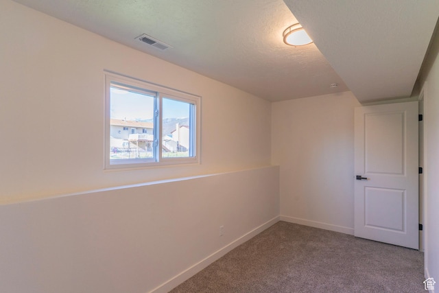 carpeted spare room with a textured ceiling, visible vents, and baseboards