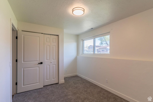 unfurnished bedroom with a textured ceiling, carpet flooring, visible vents, baseboards, and a closet