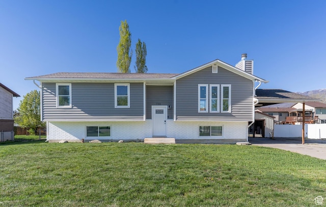 raised ranch featuring a chimney, brick siding, fence, and a front yard