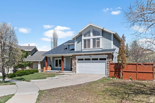 craftsman inspired home featuring fence, concrete driveway, covered porch, stone siding, and a garage