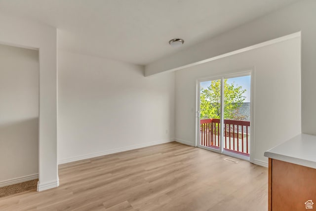 empty room with light wood-type flooring, visible vents, and baseboards