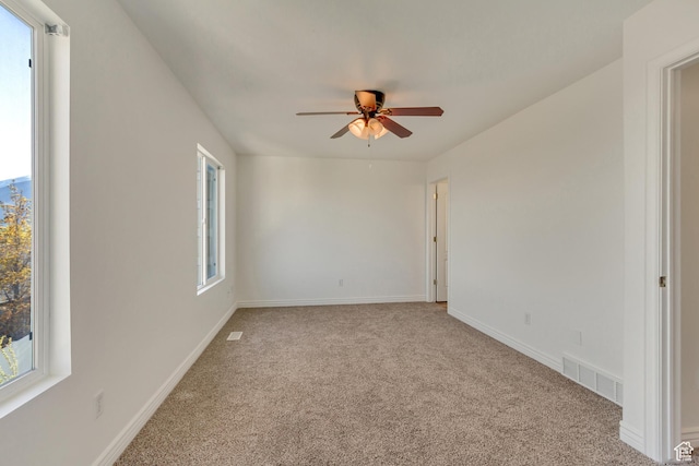 unfurnished room featuring visible vents, a ceiling fan, light carpet, and a healthy amount of sunlight