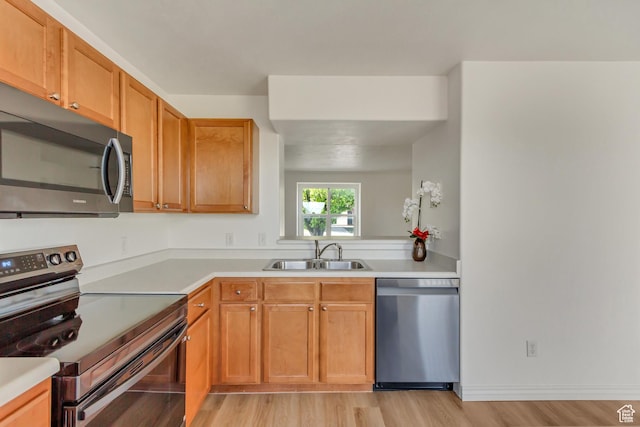 kitchen with a sink, brown cabinets, light wood-type flooring, light countertops, and appliances with stainless steel finishes