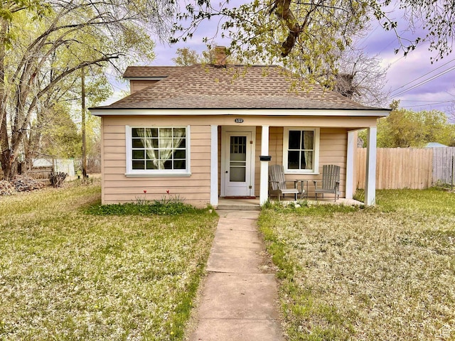 bungalow-style house with a chimney, a front lawn, fence, a porch, and roof with shingles