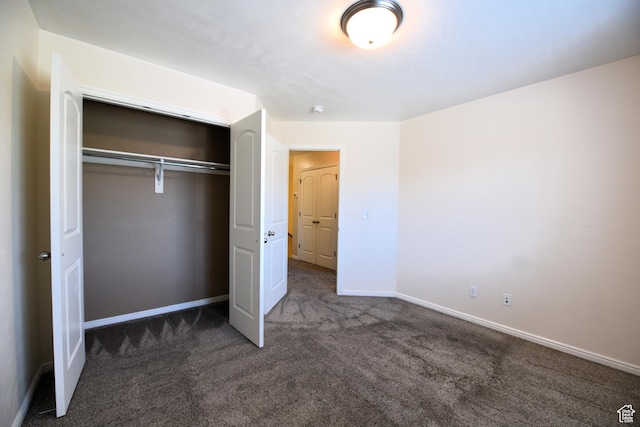 unfurnished bedroom featuring dark colored carpet, baseboards, and a closet