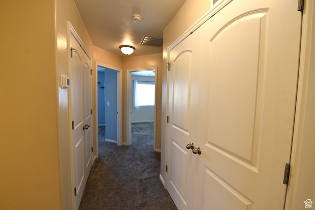 corridor with dark colored carpet, visible vents, and baseboards