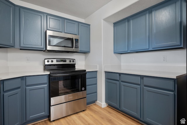 kitchen with blue cabinets, light wood-style flooring, stainless steel appliances, light countertops, and baseboards