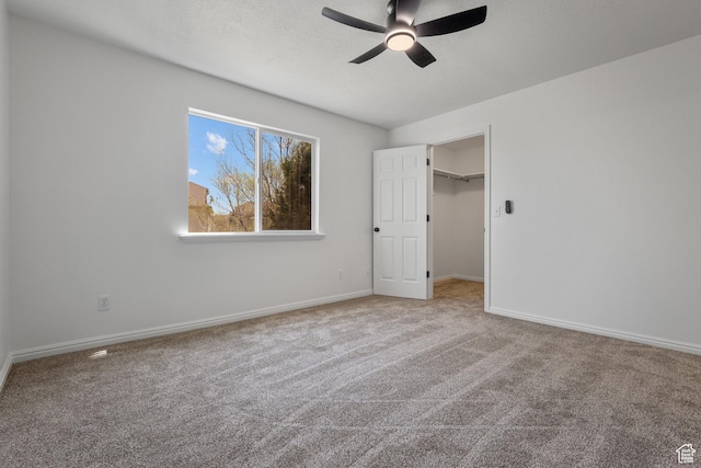 unfurnished bedroom featuring a walk in closet, baseboards, a ceiling fan, and carpet flooring
