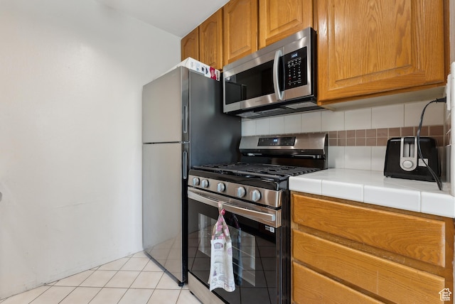 5552 S Willow Ln E Unit C, Salt Lake City, UT 84107 - kitchen featuring brown cabinets, stainless steel appliances, tile countertops, light tile patterned floors, and decorative backsplash