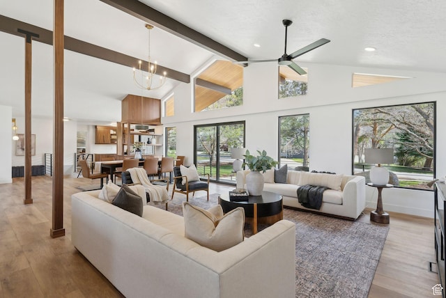 living area with plenty of natural light, light wood-style flooring, lofted ceiling with beams, and ceiling fan with notable chandelier