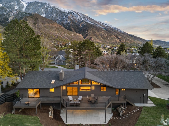 back of property at dusk featuring a chimney, an outdoor living space, a shingled roof, and a deck with mountain view