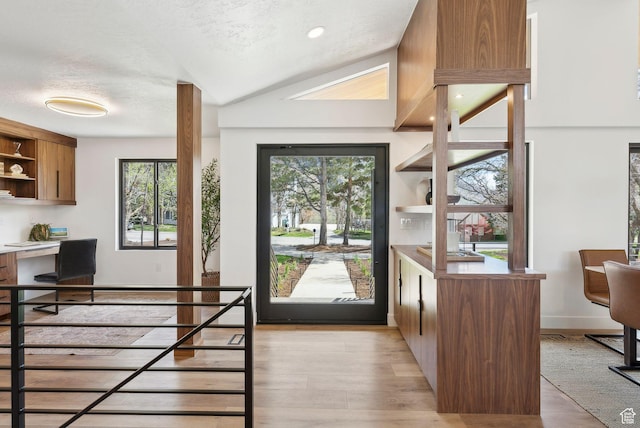 entryway with light wood finished floors, built in desk, a wealth of natural light, and a textured ceiling