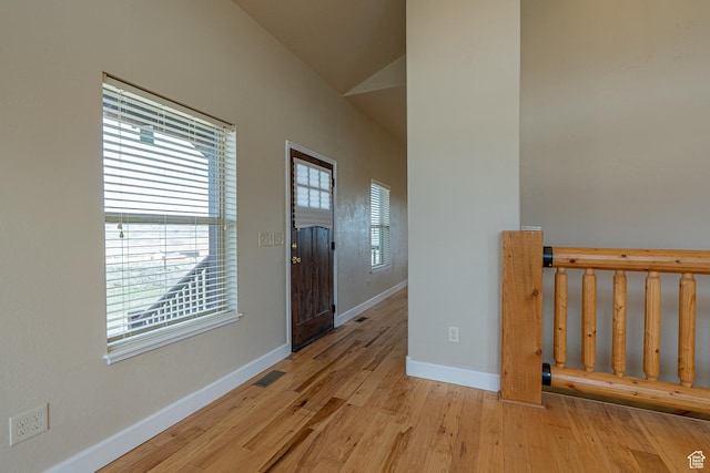 hall featuring light wood finished floors, baseboards, lofted ceiling, and visible vents