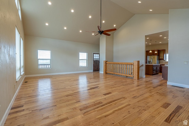unfurnished living room with baseboards, light wood-type flooring, high vaulted ceiling, and ceiling fan