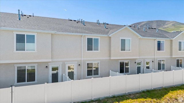 back of property featuring stucco siding, fence, roof with shingles, and a mountain view