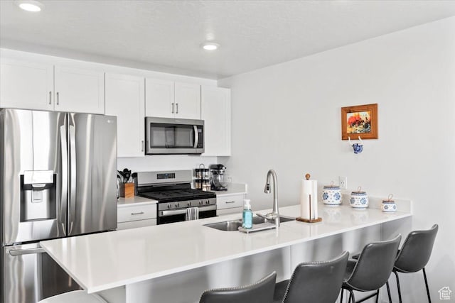 kitchen featuring light countertops, a sink, a kitchen bar, appliances with stainless steel finishes, and white cabinetry