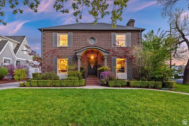 view of front of house featuring a front lawn, a chimney, and brick siding