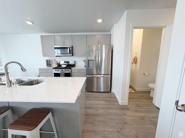 1734 E Muss Dr, Eagle Mountain, UT 84005 - kitchen with a breakfast bar, a sink, gray cabinetry, light wood-style flooring, and appliances with stainless steel finishes