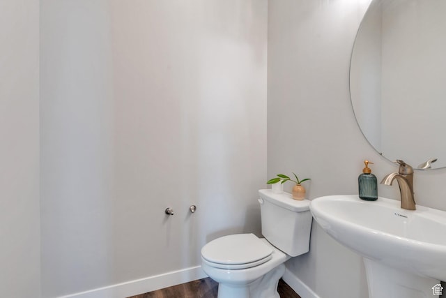 half bath featuring wood finished floors, baseboards, a sink, and toilet