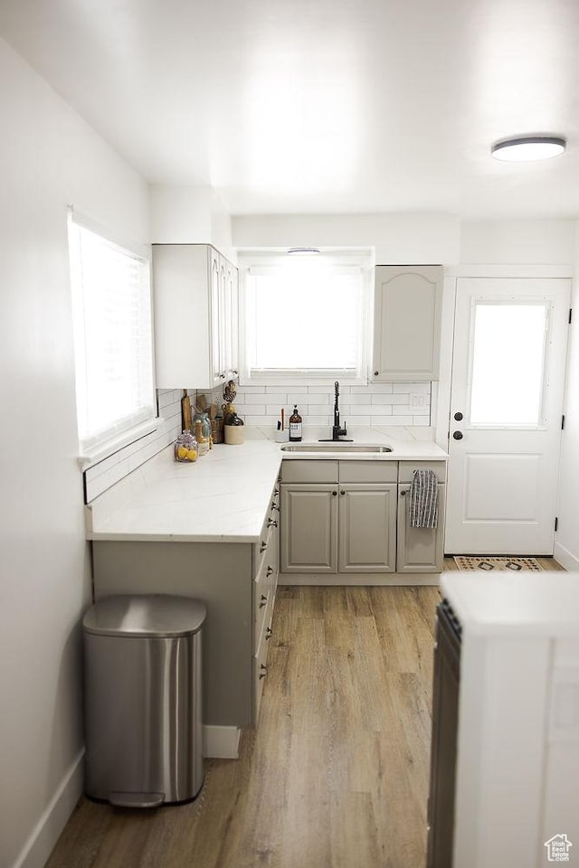 kitchen with light countertops, backsplash, gray cabinets, a sink, and light wood-style flooring