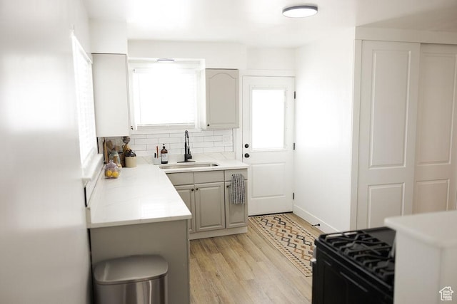 kitchen with light countertops, a sink, light wood-type flooring, decorative backsplash, and black range with gas cooktop