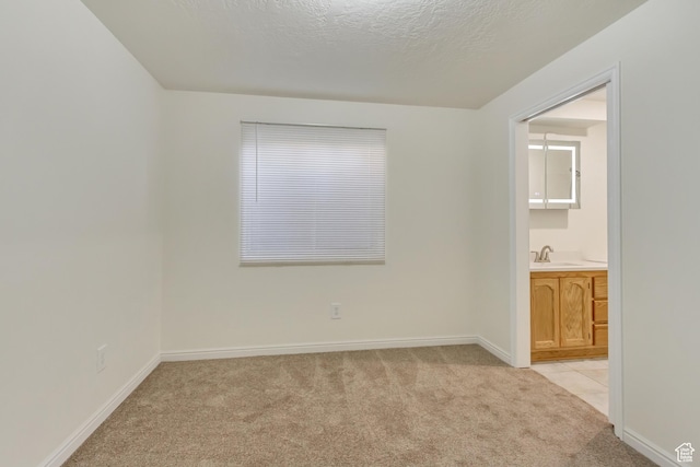 unfurnished bedroom with a textured ceiling, baseboards, light carpet, and a sink