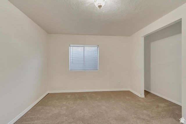 carpeted spare room featuring a textured ceiling and baseboards