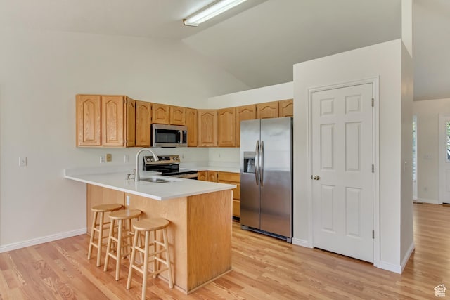 kitchen with a sink, a breakfast bar, light wood-type flooring, a peninsula, and appliances with stainless steel finishes