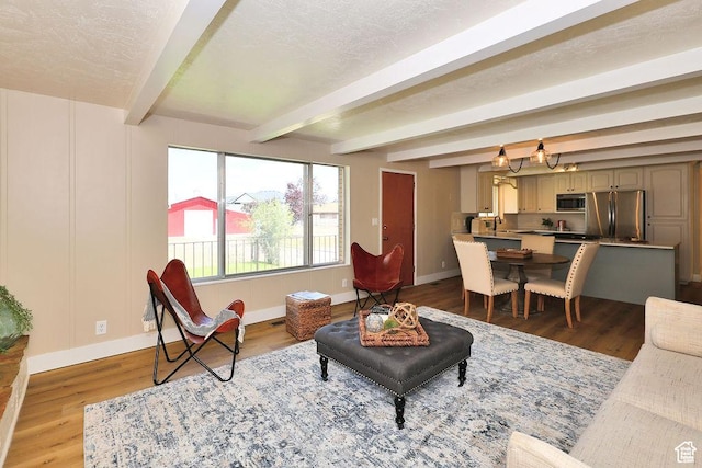 living room with wood finished floors, beam ceiling, baseboards, and an inviting chandelier
