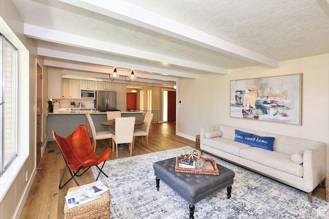 living room with light wood-style flooring, baseboards, beam ceiling, and a textured ceiling