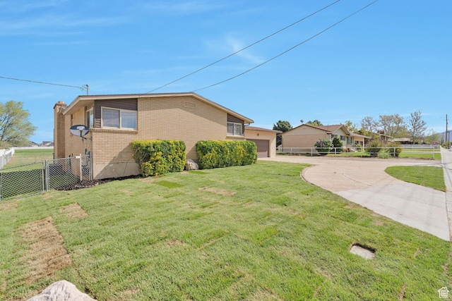view of side of home featuring fence, brick siding, a yard, and concrete driveway